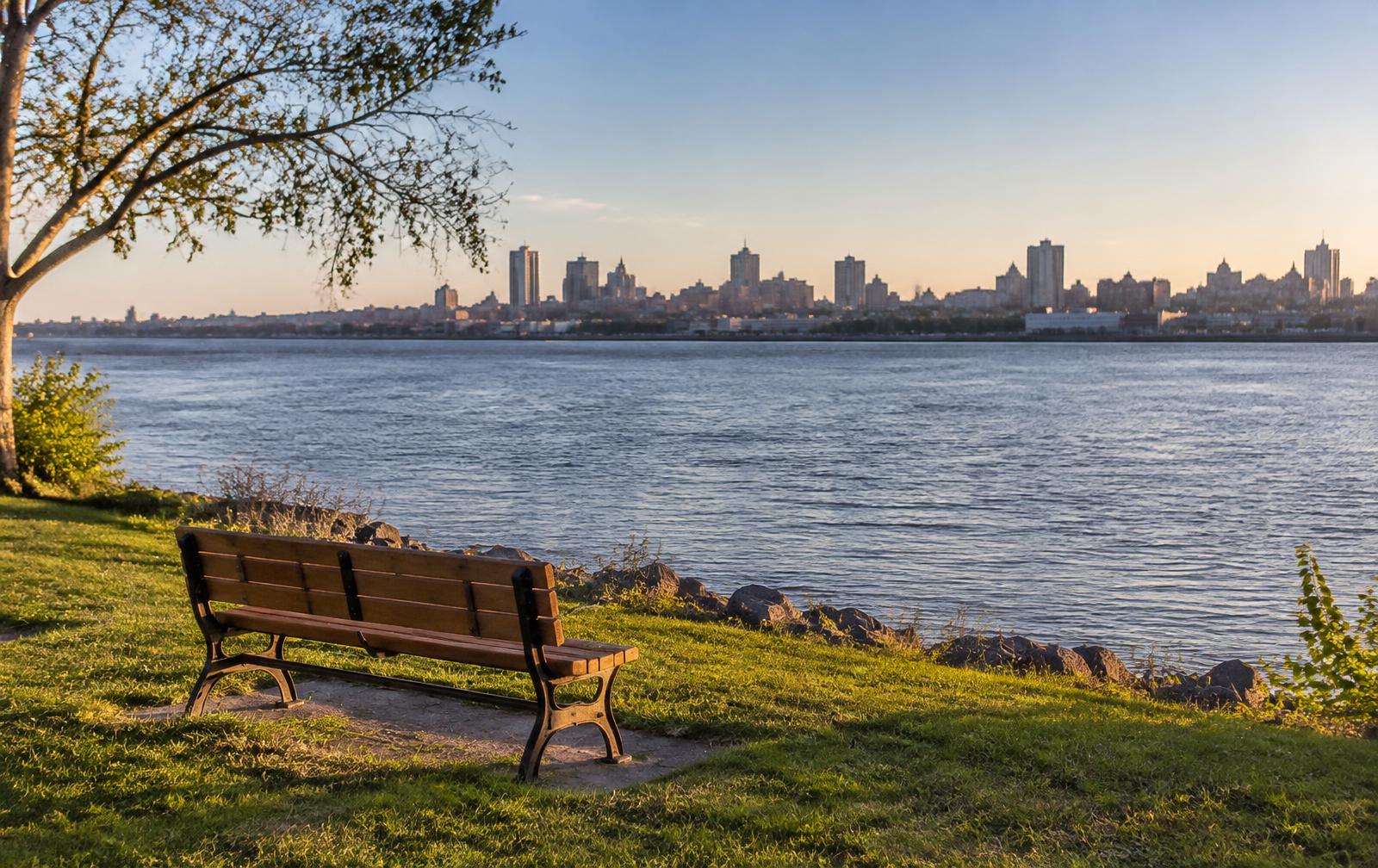 A park bench on the Catawba riverbank with the Charlotte skyline across the water